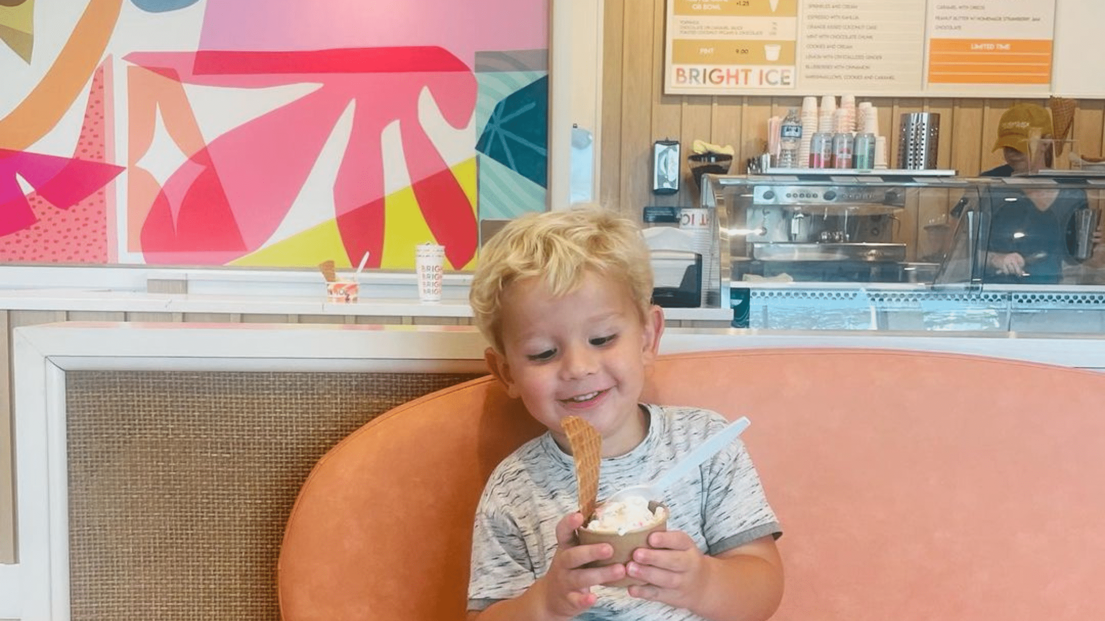 Child sitting on an orange couch smiling at the ice cream in their hand.