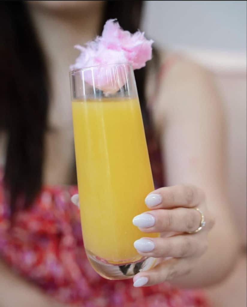 Close up of a hand holding a mimosa with cotton candy on top
