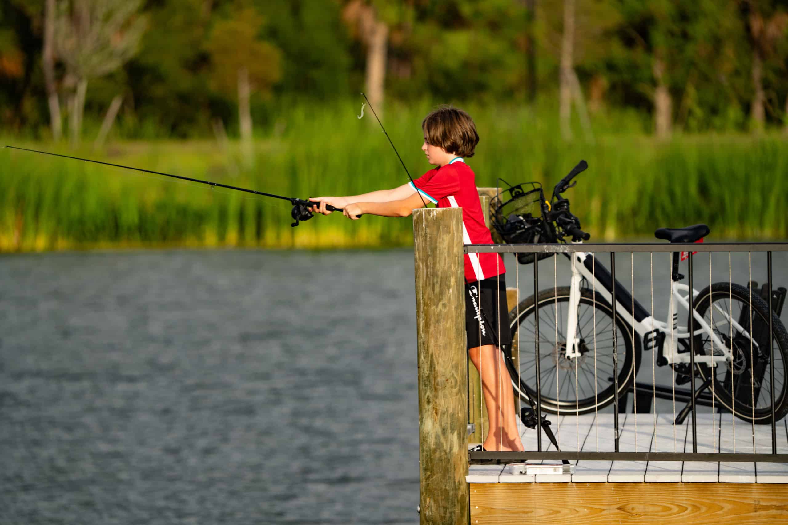 Kid leaning over a fence fishing into Grand Lake at Wellen Park Florida