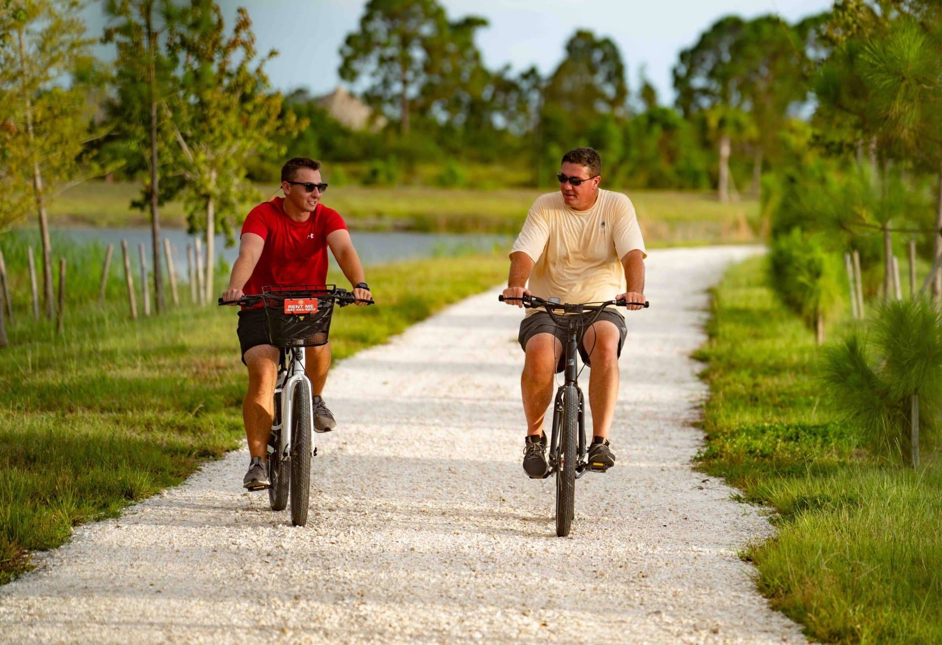 Two people riding their bikes on a trail thats right by the water and surrounded by greenery