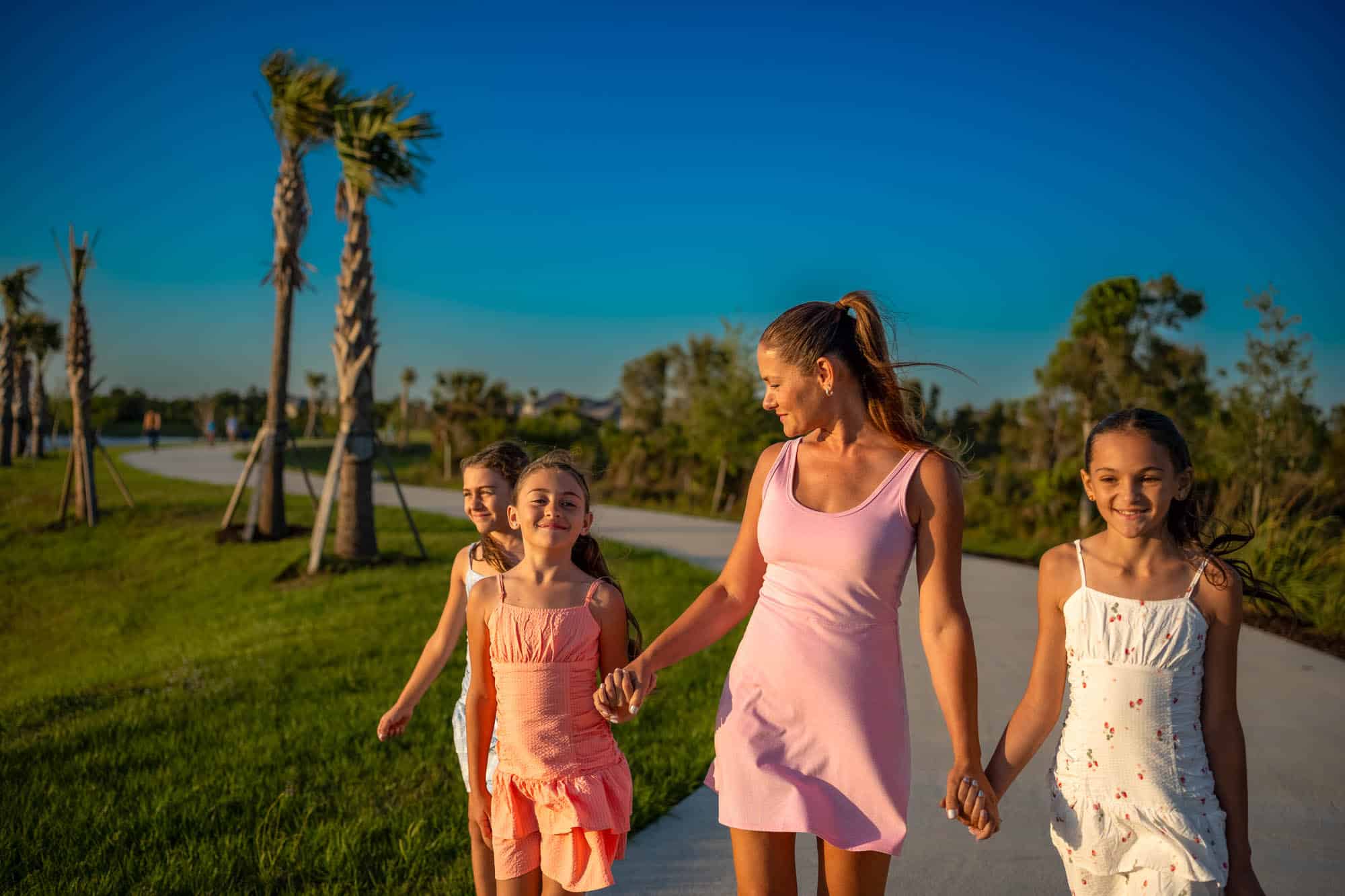 A woman and walking with three young girls in dresses walking hand in hand by the waterfront promenade