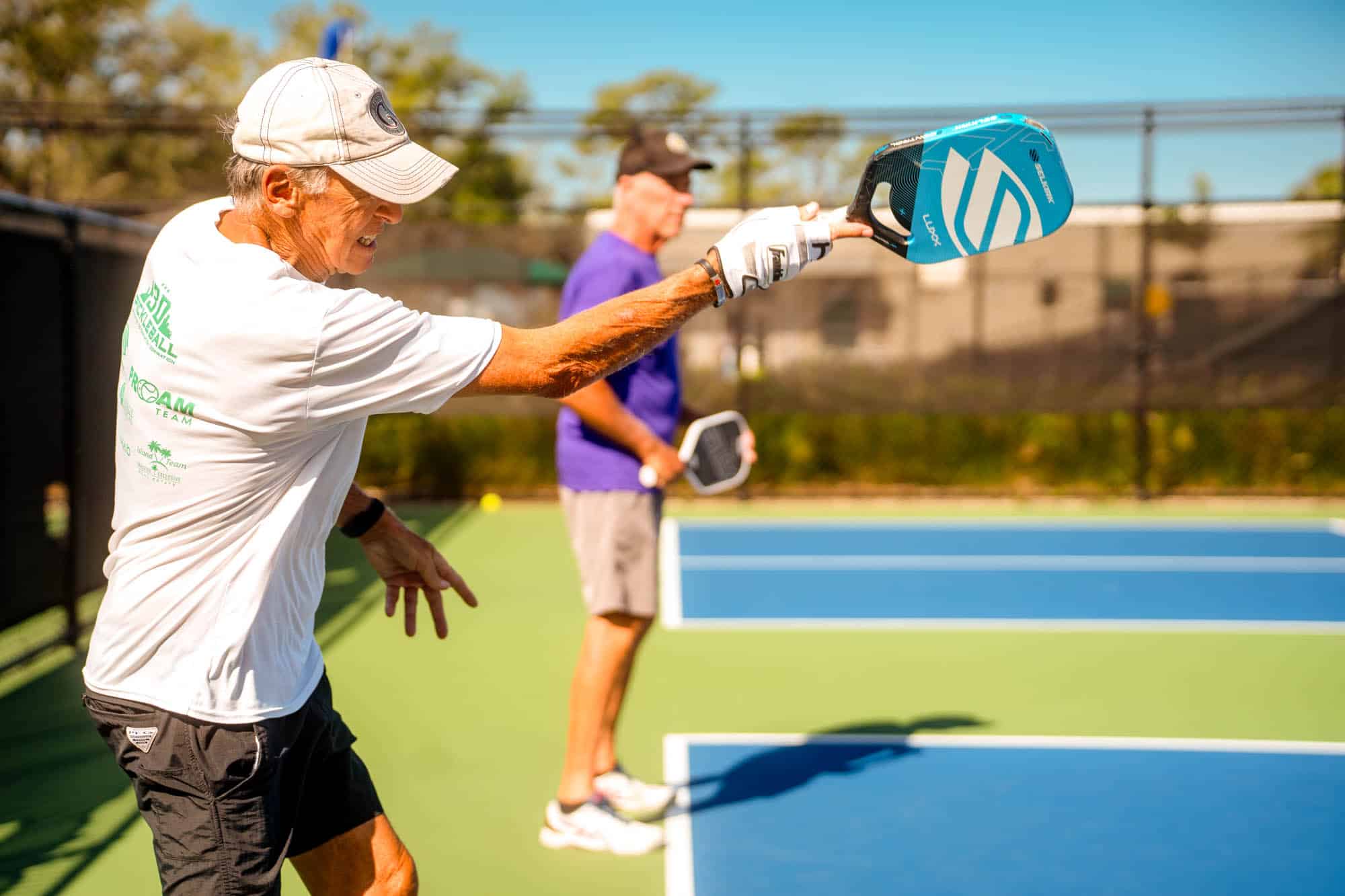 Two senior men playing paddle board on a green and blue court on a sunny day.