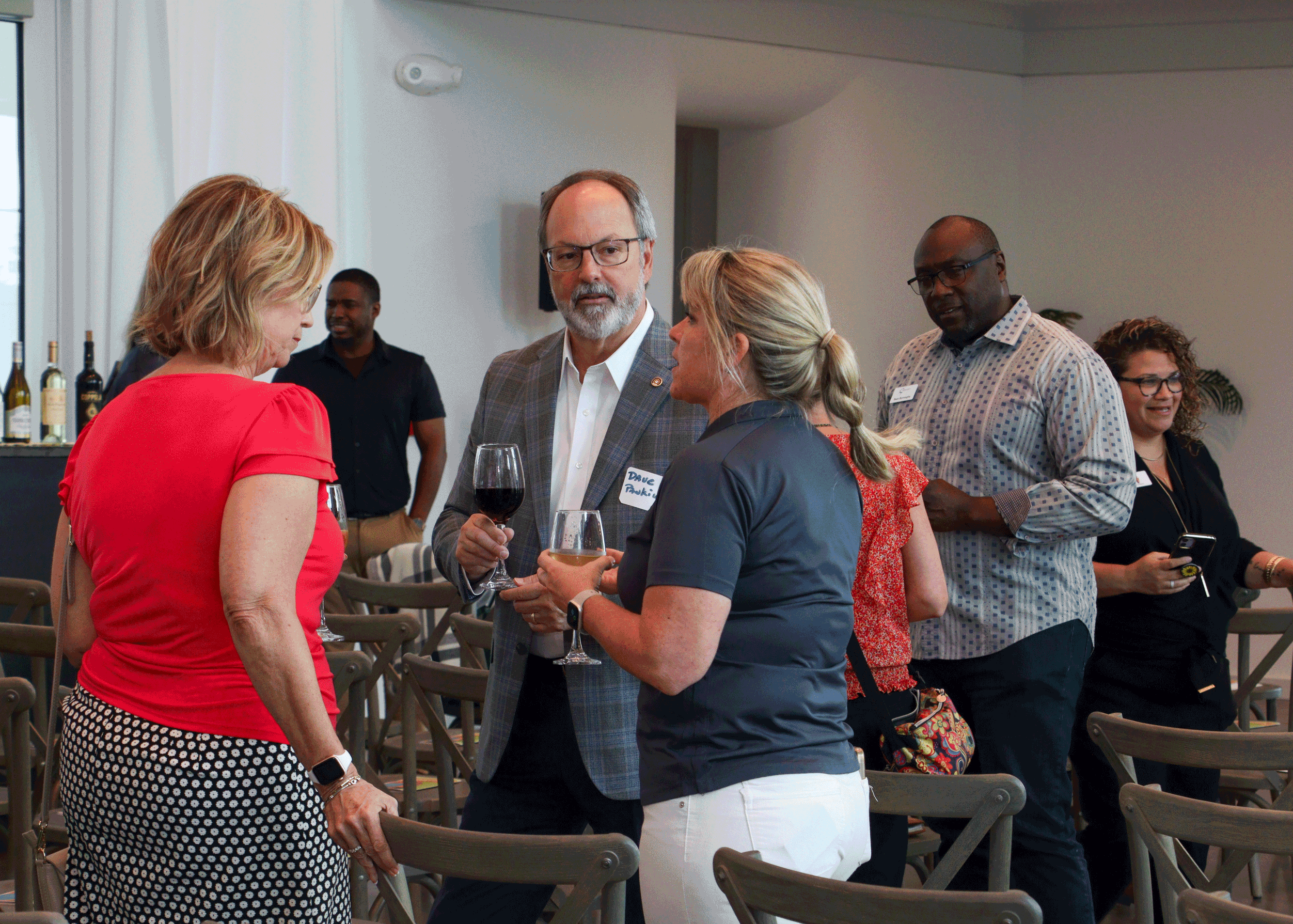 Guests mingling and enjoying drinks during a networking event, gathered in a modern venue with wine service and casual conversation.