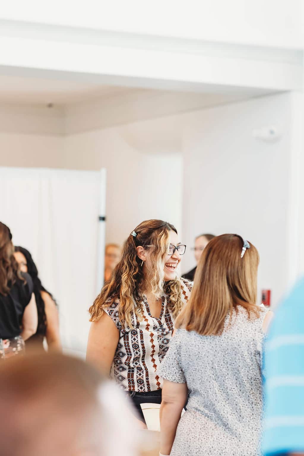 Guest smiling and chatting during a bright indoor wedding reception, surrounded by other attendees.
