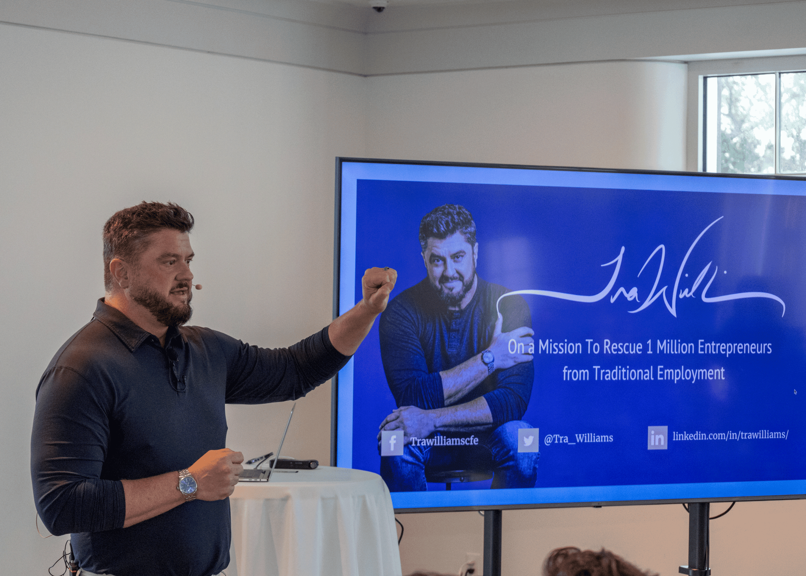 Guest speaker presenting to an audience beside a screen displaying his entrepreneurial mission and social media links at Wellen Parks corporate event venue