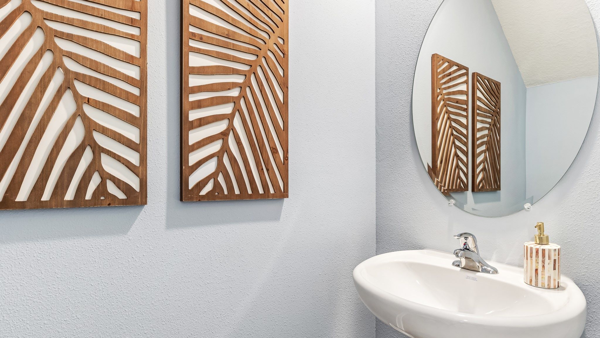 Stylish powder room with a pedestal sink, round mirror, and decorative wood wall accents, featuring clean, modern finishes.