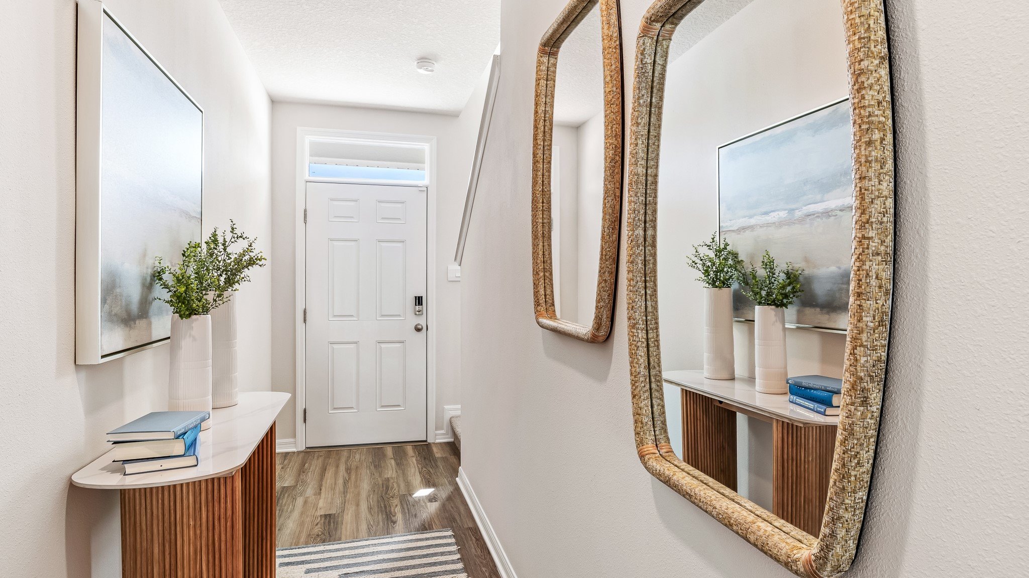Welcoming entryway with a decorative mirror, wood console table, and modern coastal-inspired accents, leading into a bright interior space.