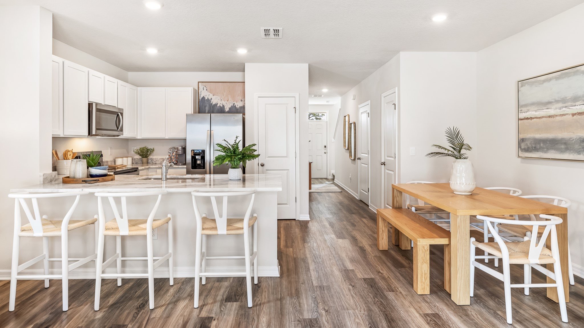 Open-concept kitchen and dining area with white cabinetry, a breakfast bar with seating, wood dining table, and modern finishes throughout.